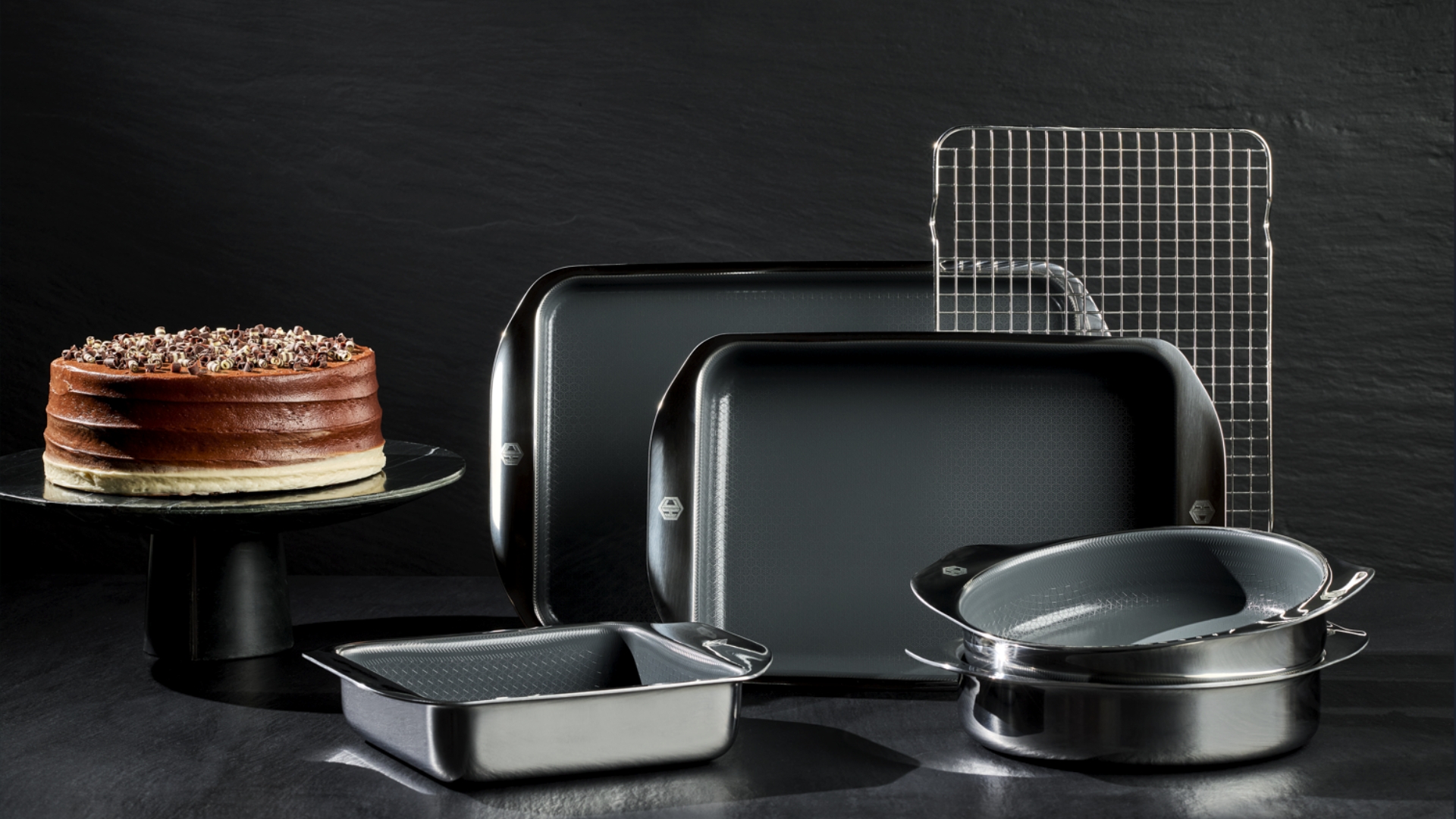 HexClad Hybrid Bakeware on a black background with a cake on a cake stand