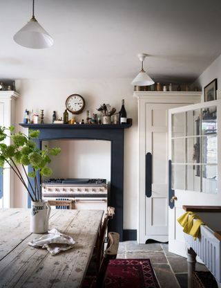 A Cream cottage kitchen with range cooker and blue overhead shelving and wooden table