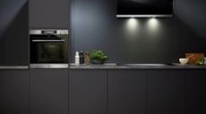 one of the best oven options in a sleek, dark hgrey and black kitchen, with dark marble surfaces, dark cabinet doors, an extractor fans with lights on the dark walls, and kitchen essentials such as salt and pepper dispensers on the worktop