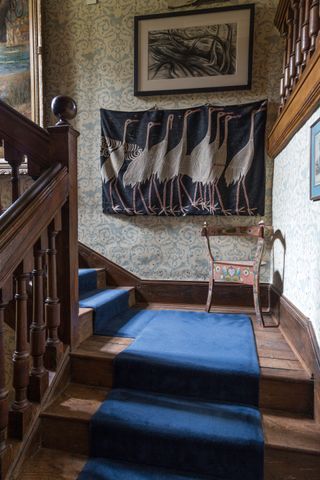 staircase in Jacobean manor with blue stair carpet floral wallpaper folk painted chair