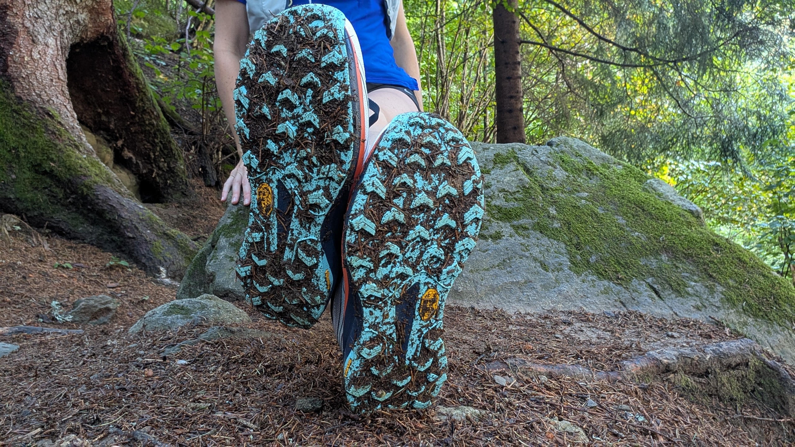 A runner sitting on a rock in a forest showing the soles of her Saucony Peregrine 16 trail shoes