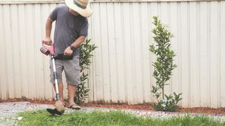 A man in a sun hat edging a lawn with a lawn edger tool