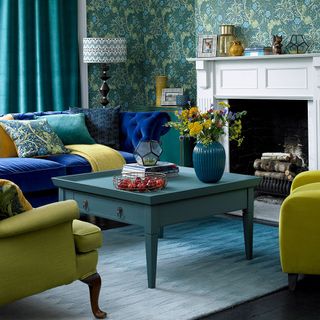 Blue themed living room with flowery wall paper, blue sofa and a while fireplace