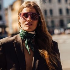 woman wearing a green silk scarf, brown blazer, and purple glasses