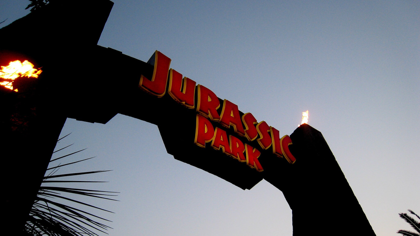 An arch with fiery torches reads &quot;Jurassic Park&quot; in red lettering