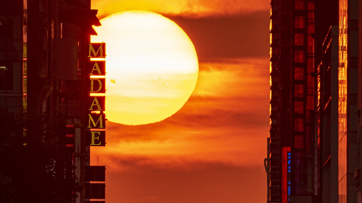 The sun is pictured emerging peeking around the high-rise buildings of New York's 42nd Street