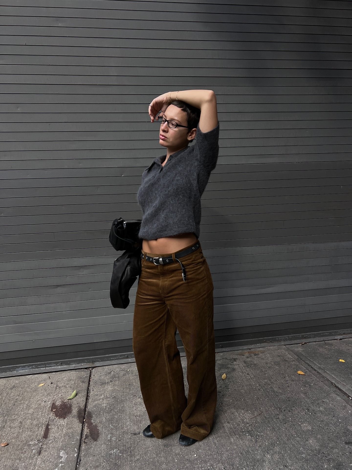 Influencer Aïsha Farida in a dark heather polo sweater, brown corduroy pants, studded belt, and black shoes.