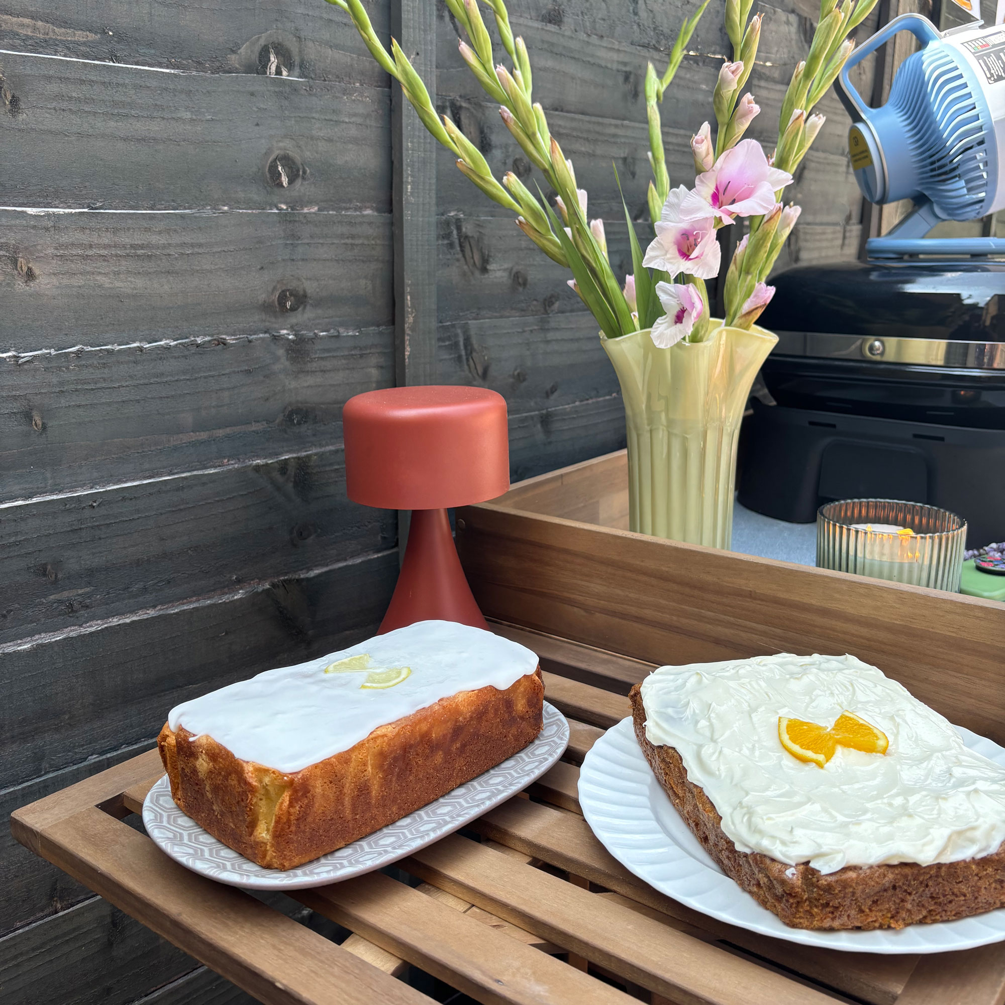 Wooden bench with carrot cake and lemon drizzle cake next to a red table lamp