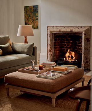 Living room with a fireplace, sofa, table lamp and large ottoman upholstered coffee table