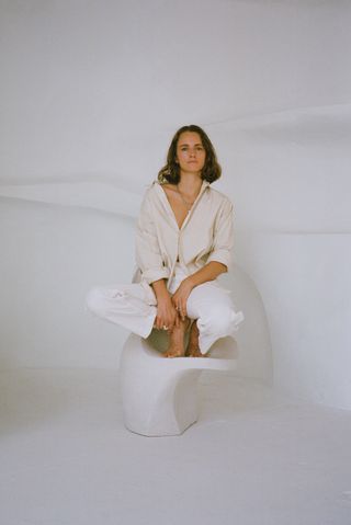 Simone Bodmer Turner crounching on a cream ceramic chair she designed