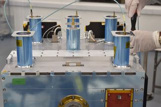 The vessel containing Celestis flight capsules is attached to the orbital test bed, located between the blue cylinders.