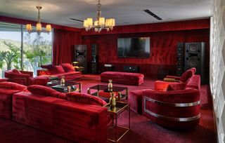 A media room with a large sound system, a wall mounted TV, and red velvet upholstery