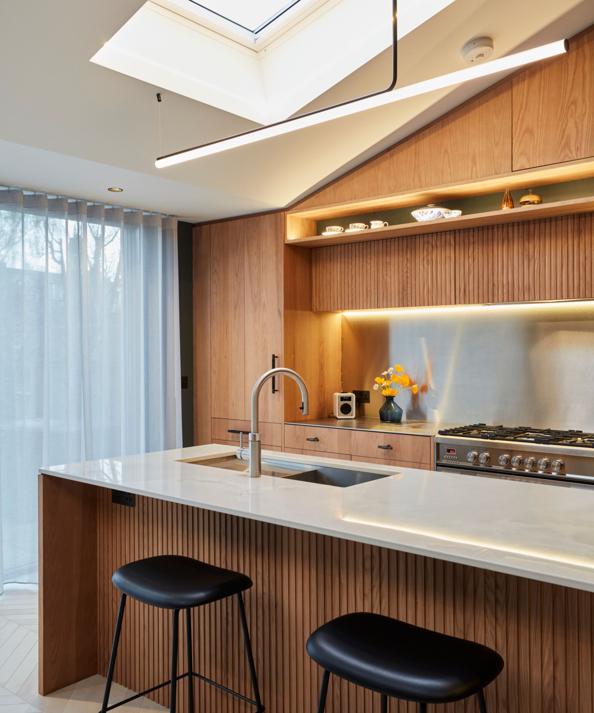 A contemporary kitchen with warm wood cabinetry, a fluted island, skylight and layered lighting for a calm, design-led cooking space.