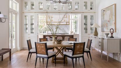 a large white and light breakfast area off of a kitchen with a walk through bookcase, round table and black and rattan chairs