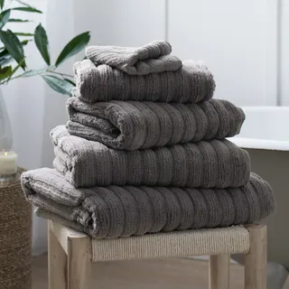 A pile of ribbed fluffy grey towels on a wooden and woven stool in a white bathroom