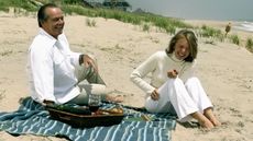 still image from the Nancy Meyers movie Somethings Gotta Give of two characters sat laughing on the beach with a striped towel and picnic