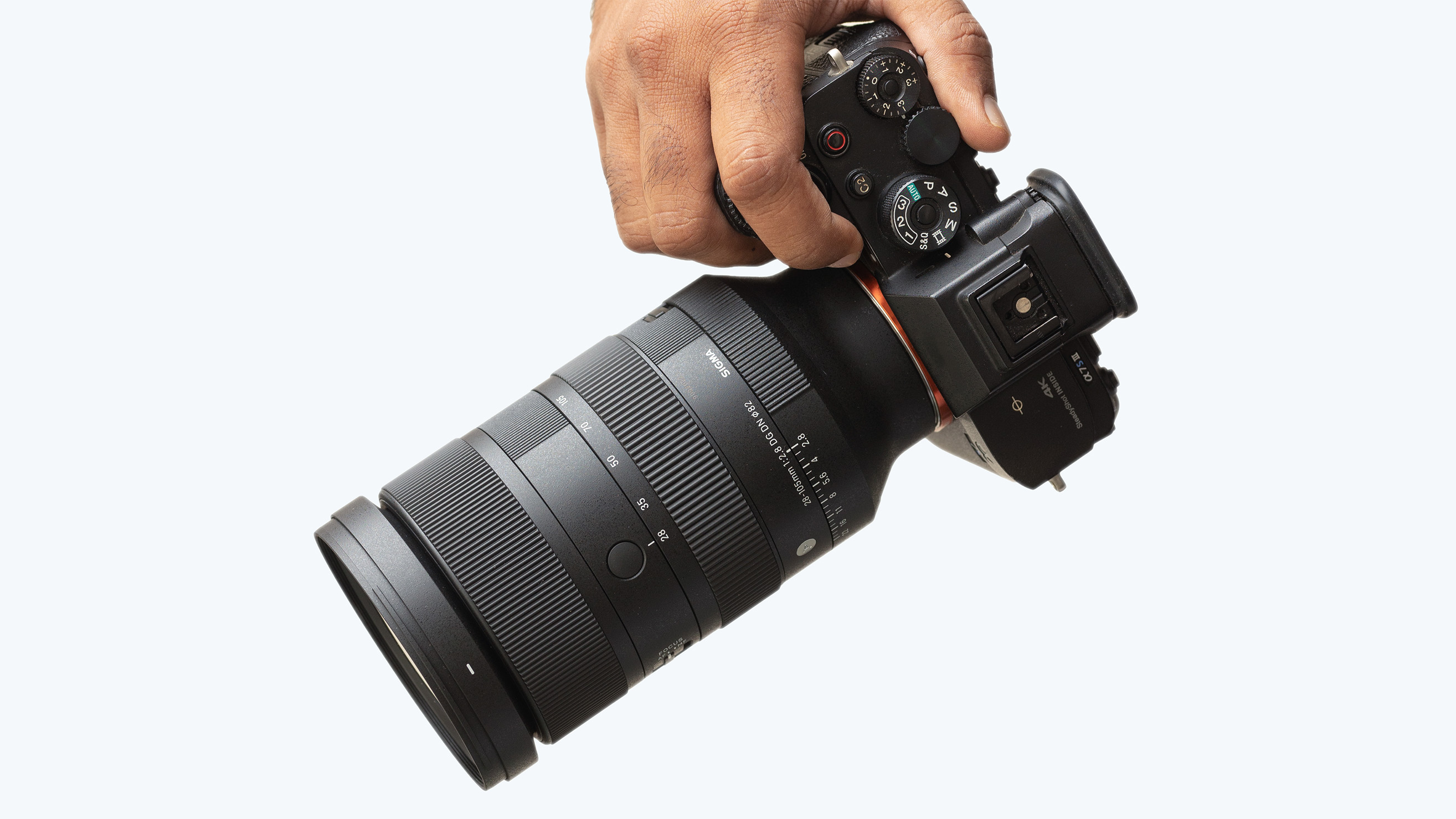 Sigma 28-105mm f/2.8 DG DN Art on a Sony camera, being held against a grey background