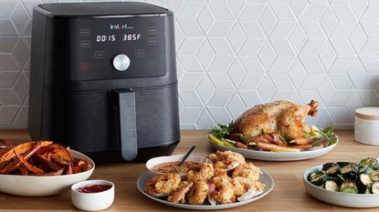 Instant Vortex air fryer on kitchen counter with geometric tiles and assortment of cooked foods