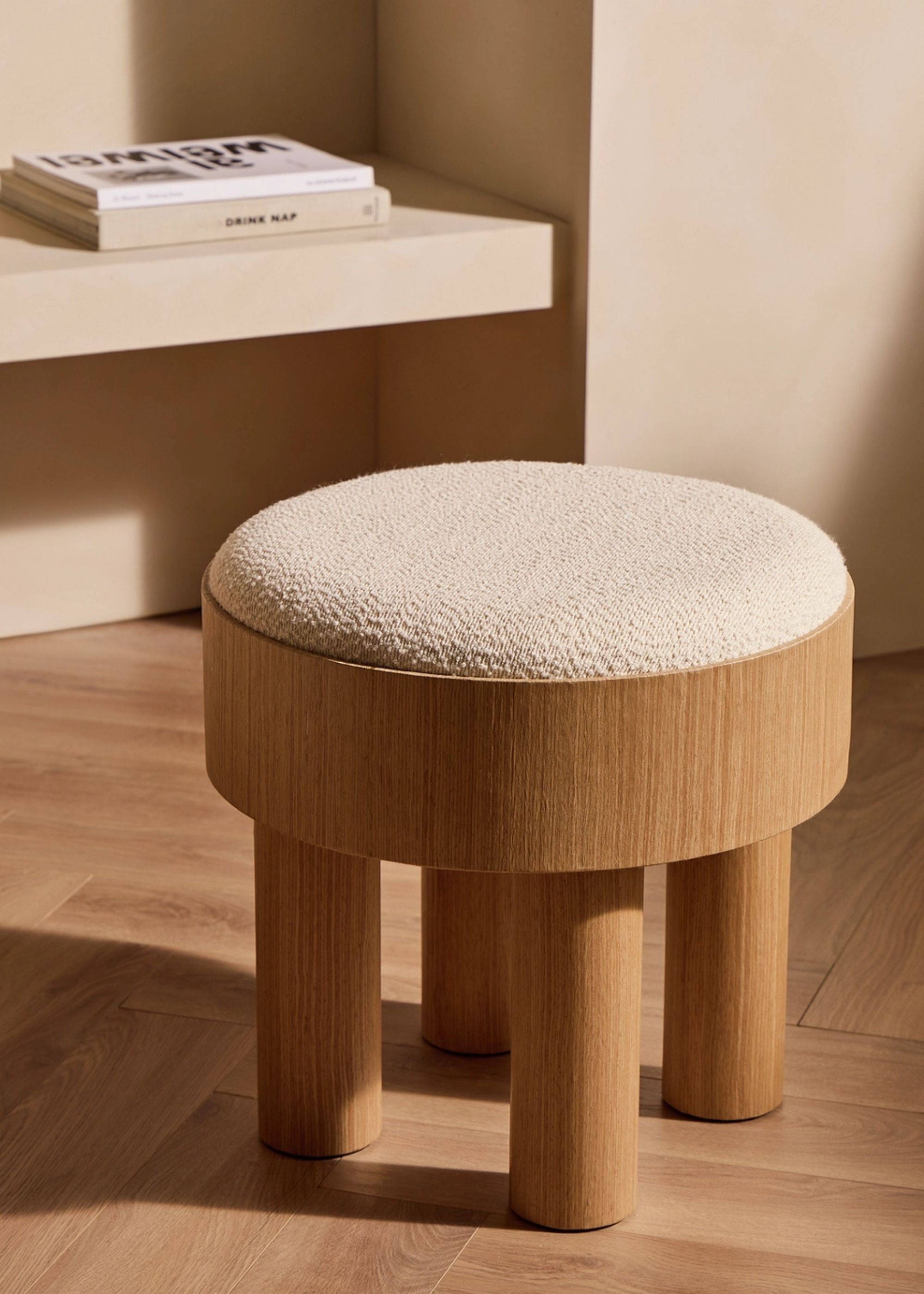 Image of a wooden footstool with a white boucle top in a beige room with wooden flooring.