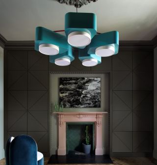 A living room with dark grey walls and a turquoise lighting piece