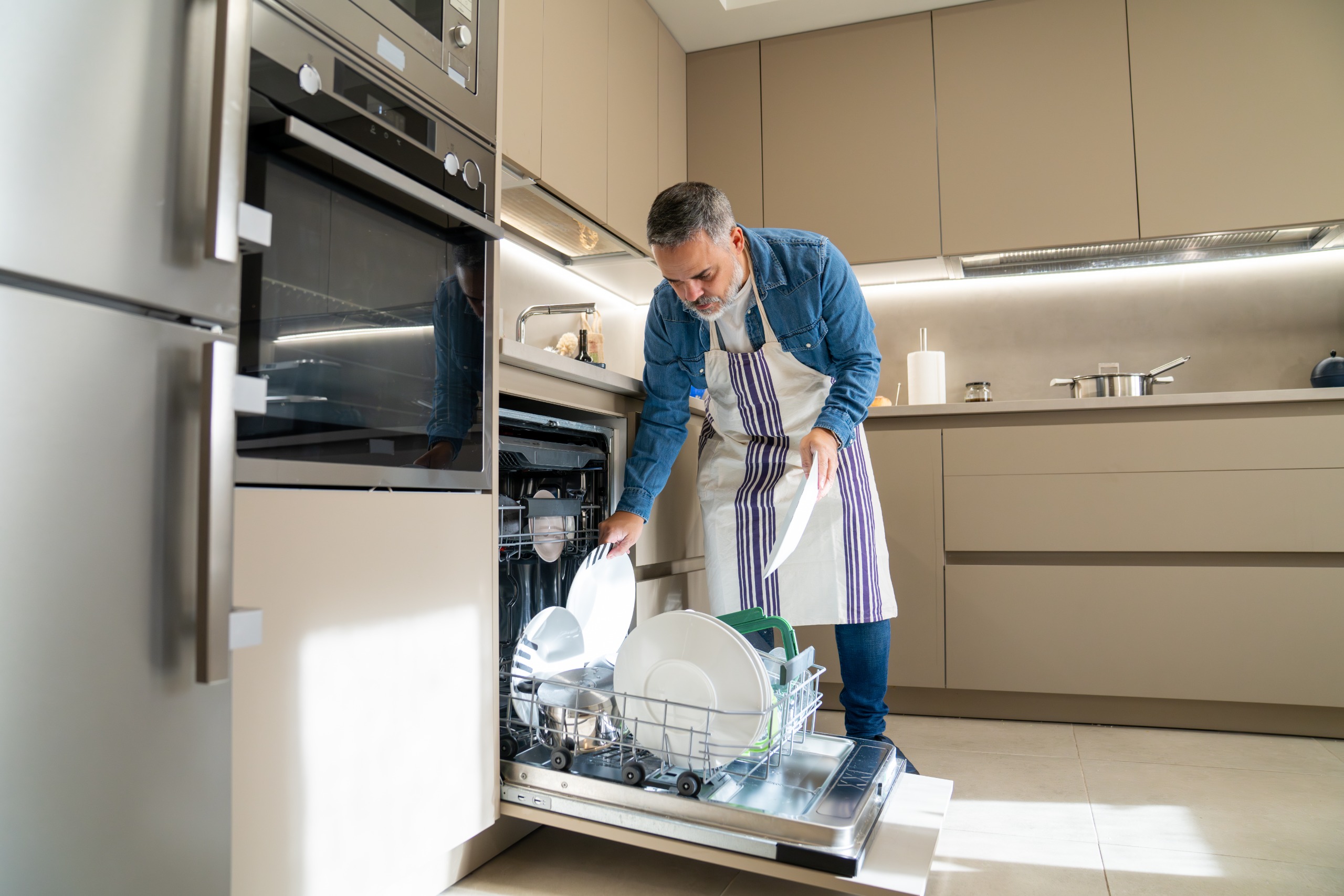 A man loads dirty dishes into his dishwasher.