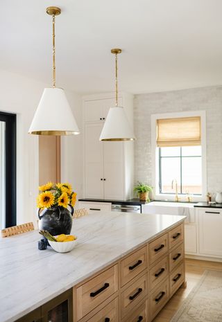 white kitchen with wooden island with marble countertop and white cabinetry with dark soapstone countertops sunflowers on island and two white and gold pendant lights