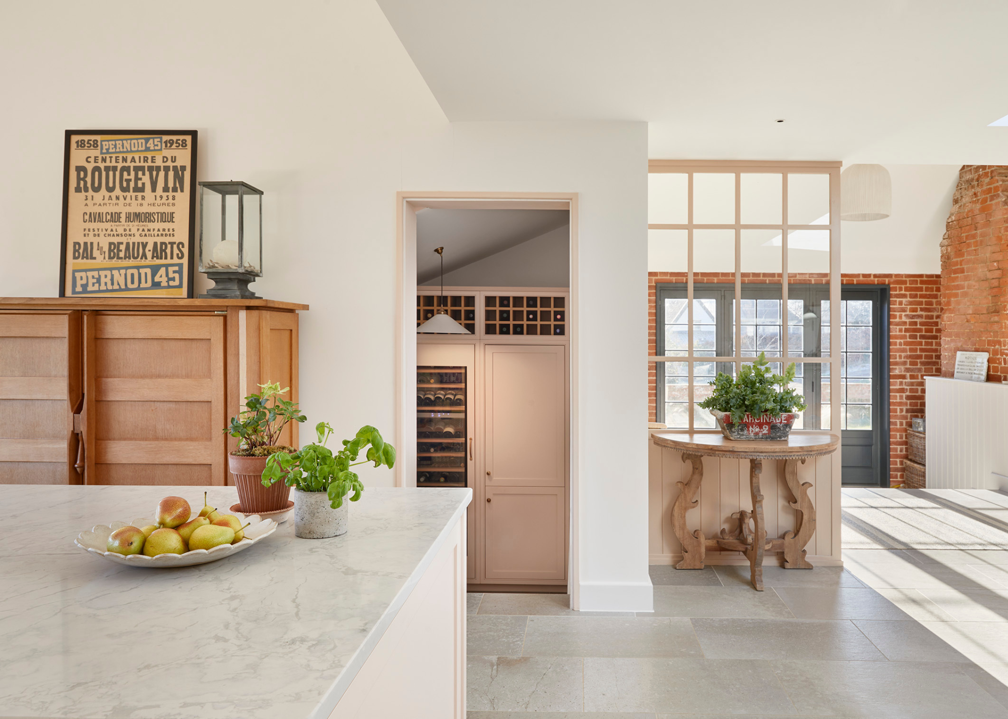 A white kitchen with light pink and red brick featuring throughout the space, including into a walk-in pantry where you can see wine stored
