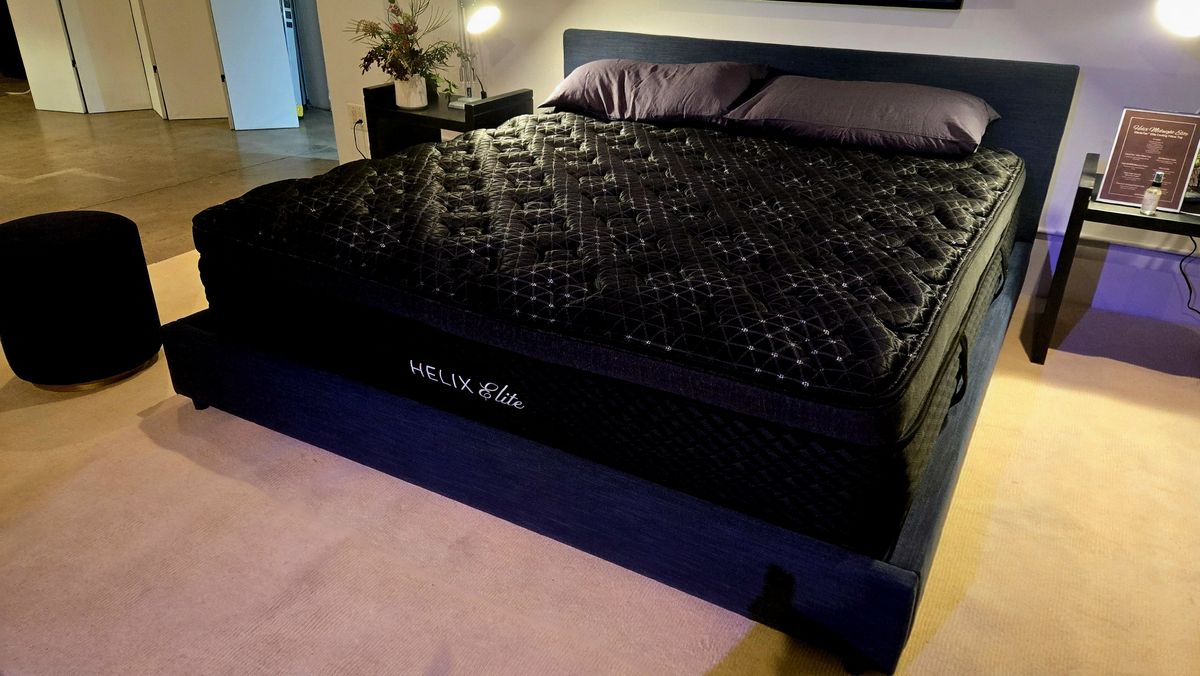 Angled shot of the new Helix Midnight Mattress on a black bed frame with a couple of pillows on top