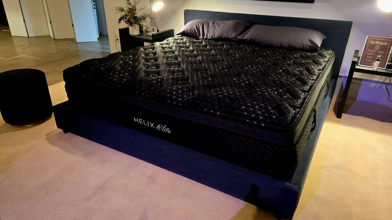 Angled shot of the new Helix Midnight Mattress on a black bed frame with a couple of pillows on top