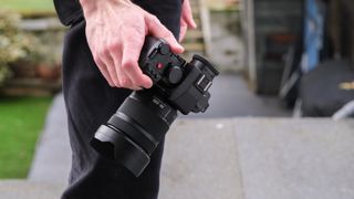 Panasonic Lumix S 28-200mm attached to a camera held in a hand down by a side