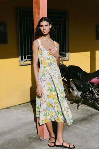 A model leans against a pole wearing a white midi dress with lemon print and black sandals from zara