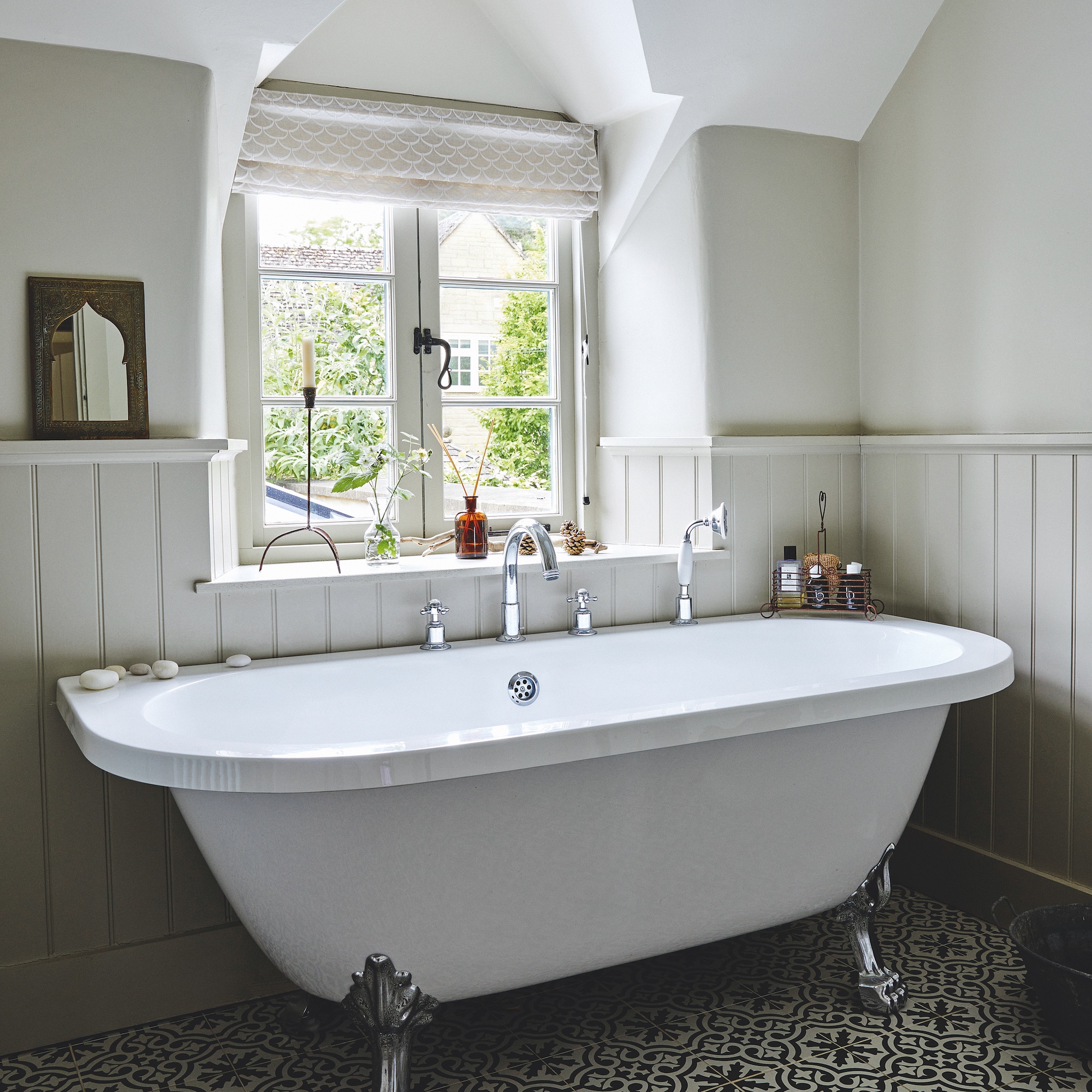 cottage bathroom with white bath beneath window and tongue and groove panelling on walls and patterned floor tiles