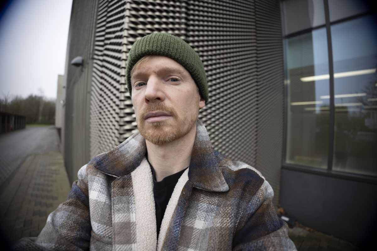 A man in a green beanie and jacket's selfie, outdoors in gray urban area