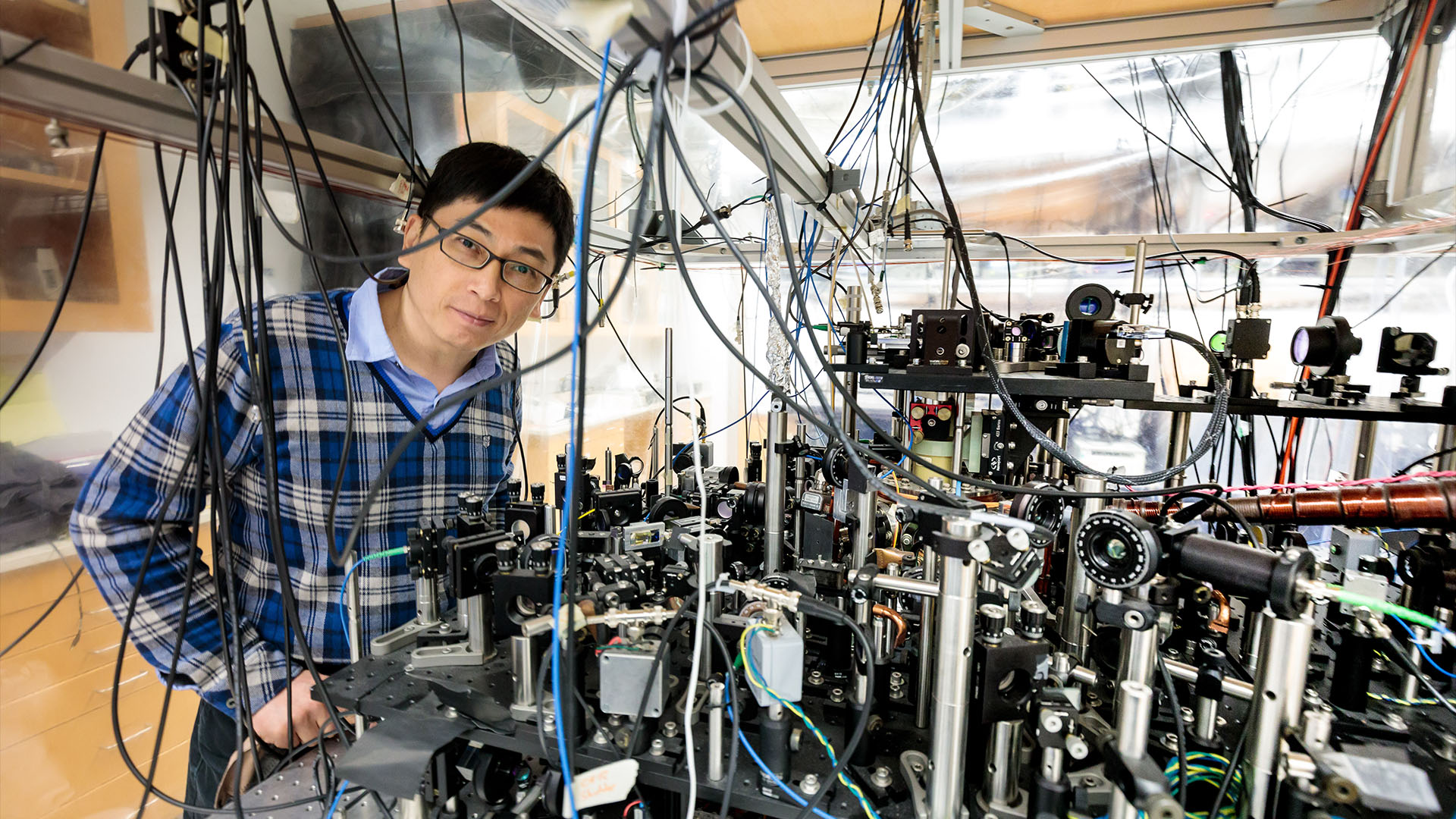 Cheng Chin poses with the apparatus used to trap cesium atoms and convert them to cesium molecules using quantum superchemistry.