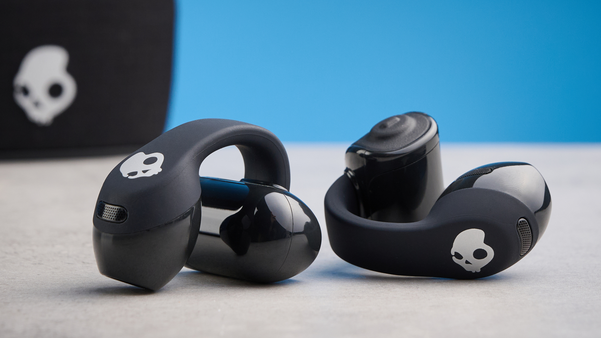Skullcandy Push 720 Open in black and silver colorway with charging case photographed on a blue background