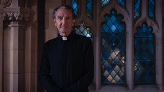 Anton Lesser in a black jacket and white dog collar as Father John.