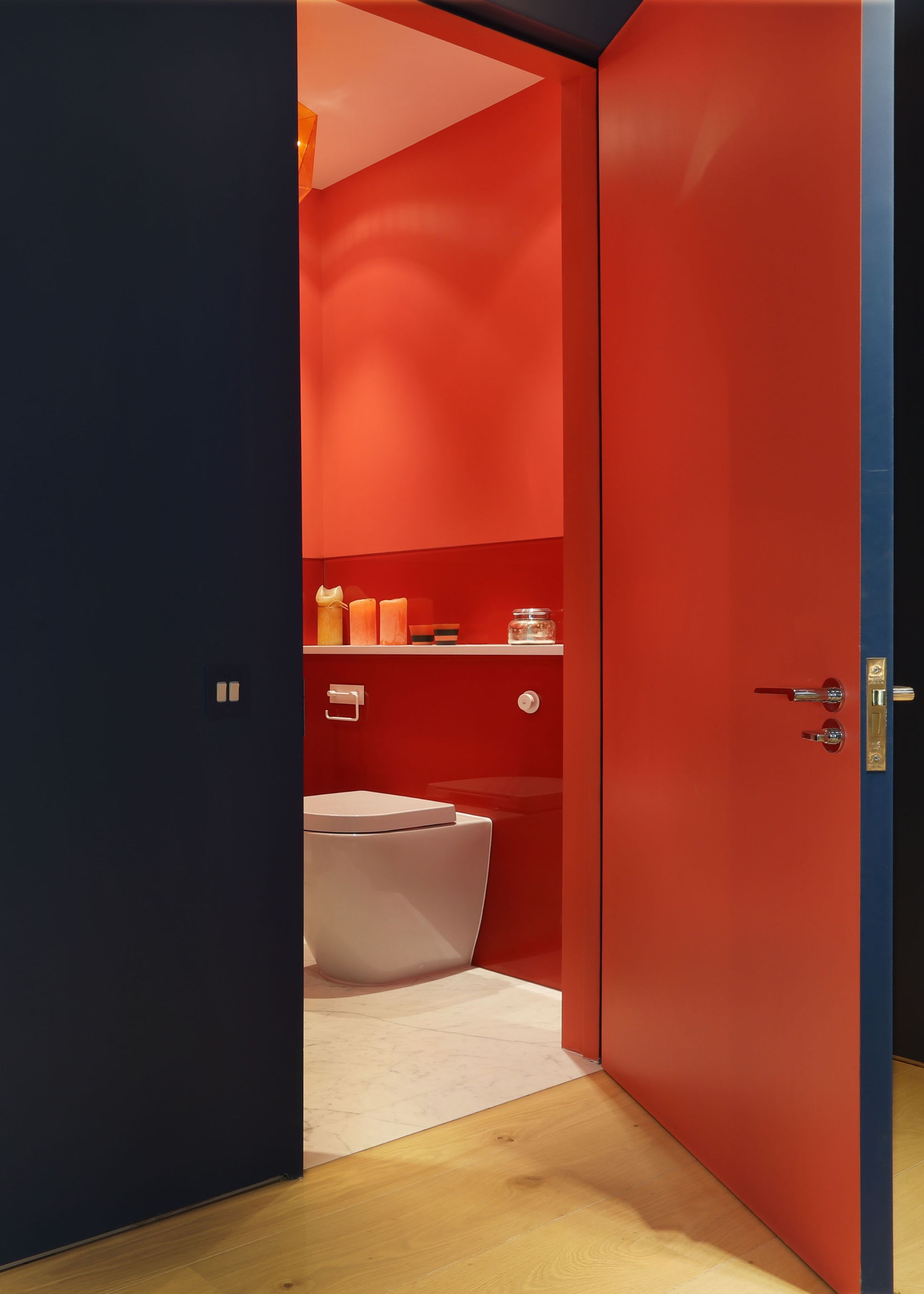 A bathroom painted red with the exterior door and walls outside of the bathroom painted dark navy/blue