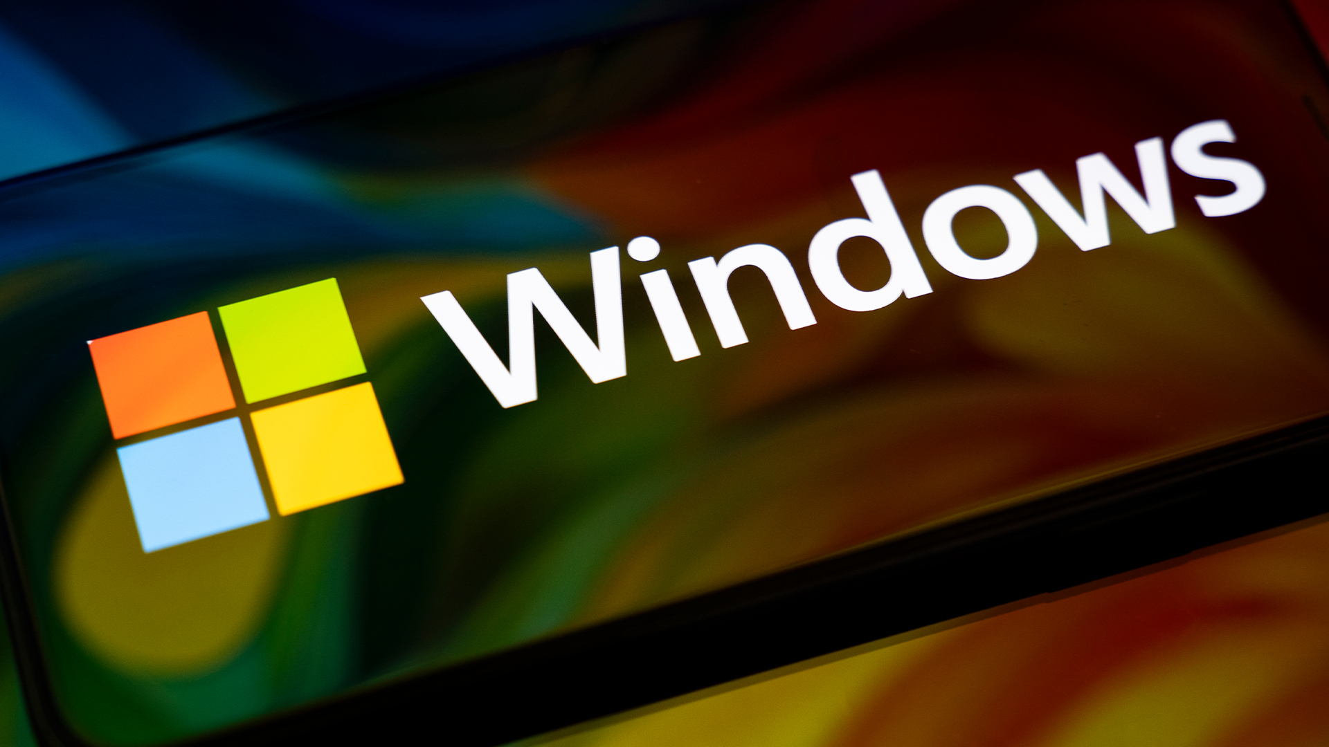 Logo and branding of Windows, Microsoft's desktop and laptop operating system, on a smartphone screen with flowing multi-colored graphics blending into screen and background.