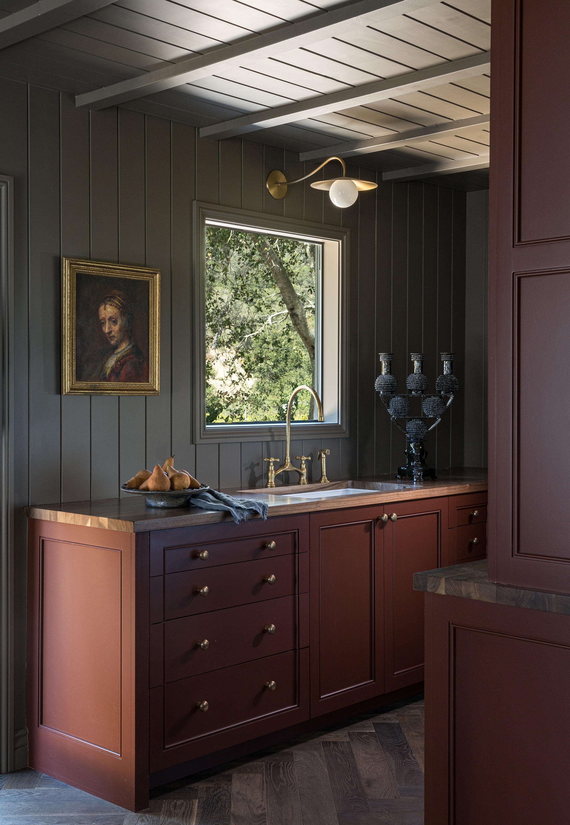a dark red kitchen with paneling on the walls and ceilings, with a golden-framed classic painting on the wall
