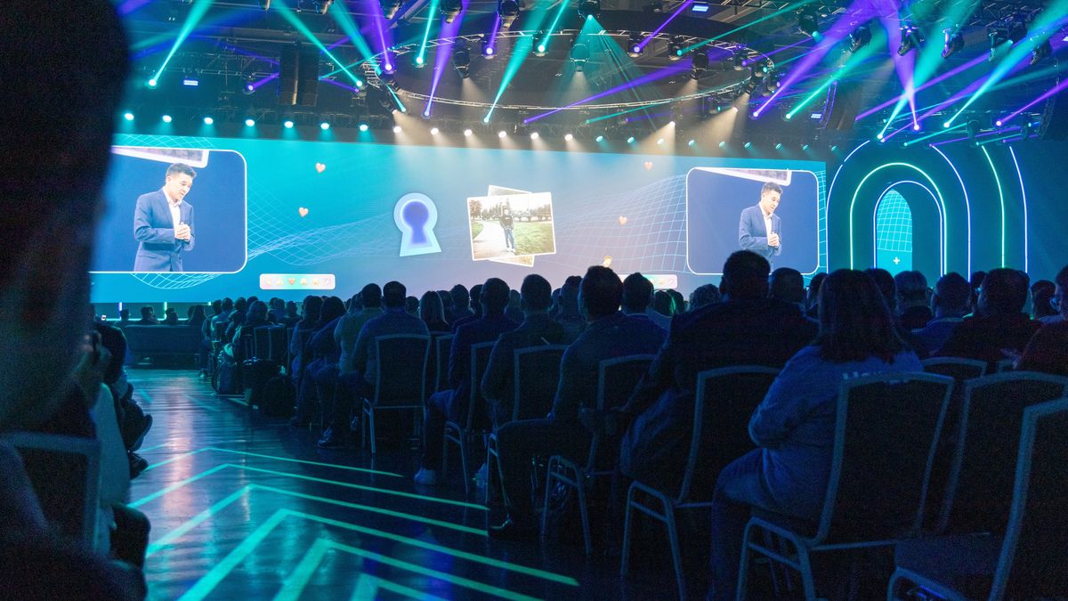 A man speaking on stage projected onto a screen.