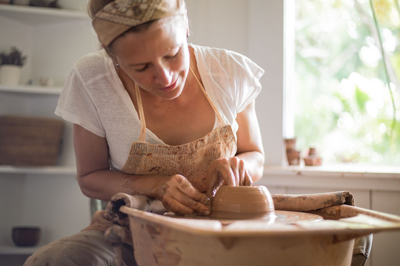 A woman on sabbatical reworks a thrown pot on a potter&#039;s wheel.