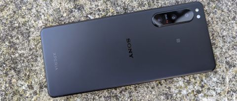 A black Sony Xperia 5 IV being held above and laid on a stony surface