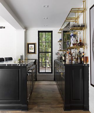 A home bar with black cabinetry and brass shelving