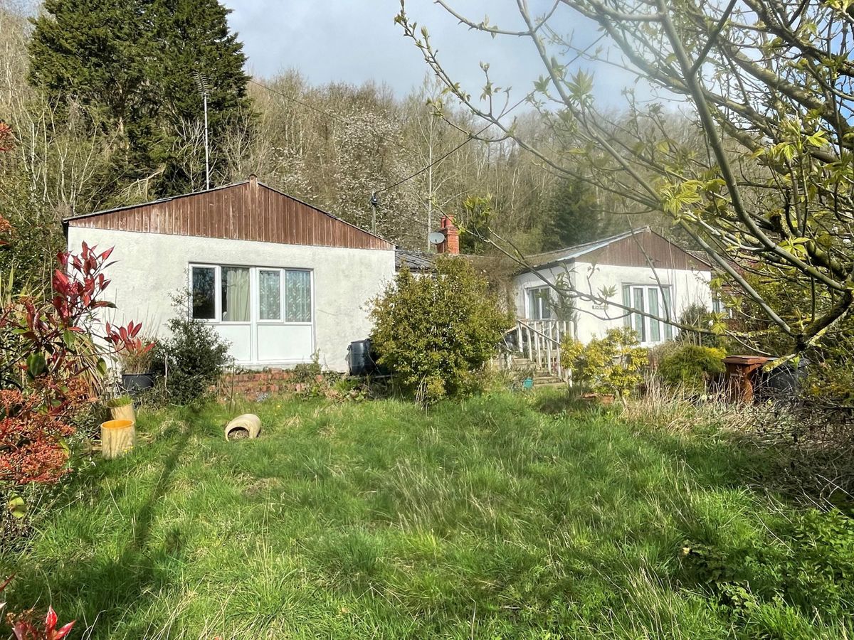 The front garden of a shabby bungalow is overgrown