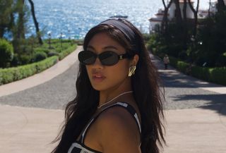 Woman wearing black Celine sunglasses, black headband, gold earrings, and white and black dress in the South of France.