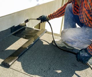 tradesperson applying heat with torch to bitumen felt roof covering