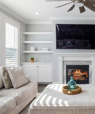 Neutral living room with white shelves, TV on the wall above the fireplace and upholstered cream sofas and coffee table