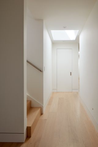 An all white narrow hallway with wooden floor