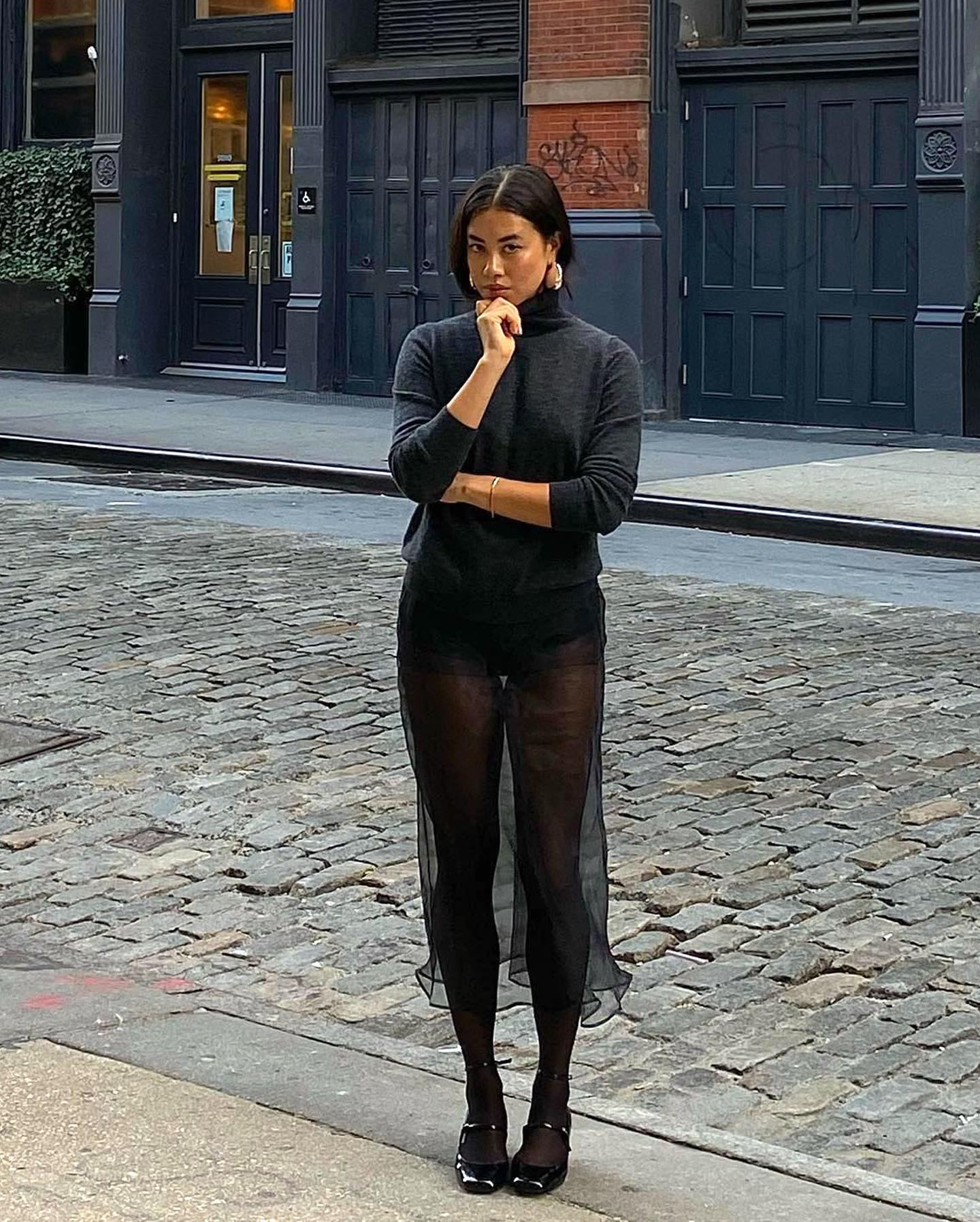 fashion influencer Sasha Mei posing in a gray turtleneck sweater and black sheer skirt