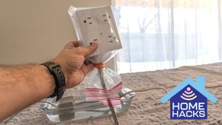 A surge protector wrapped in a plastic bag to protect its outlets with part of its braided cable submerged in water in the background